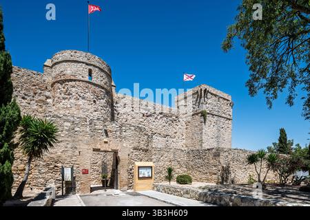 I visitatori ammirano lo storico castello di Santiago a Sanlucar de Barrameda, in Spagna, contro un cielo azzurro e una vegetazione vivace. Foto Stock