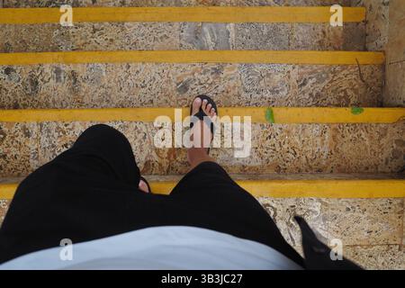 POV. Dopo la pioggia, la persona cammina lungo le scale bagnate in pietra contrassegnate da strisce gialle luminose. Foto Stock