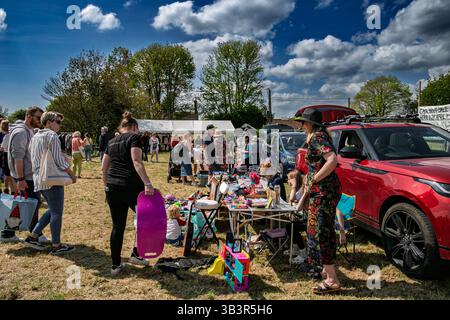 Una vivace vendita di stivali per auto all'aperto con persone che navigano tra le bancarelle e una vivace auto rossa parcheggiata nelle vicinanze in una giornata di sole Foto Stock