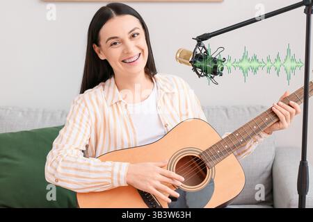 Giovane donna con microfono che suona la chitarra in studio di registrazione Foto Stock