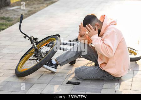Giovane con il cellulare rotto dopo essere caduto dalla bici nel parco Foto Stock