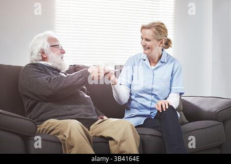 Il paziente anziano ha il tè con un infermiere e un assistente medico amichevole. Operatore sanitario che serve il cliente maturo con un sorriso. Assistenza da parte dell'operatore sanitario Foto Stock