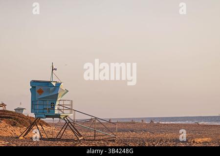 La torre del bagnino sorveglia la tranquilla spiaggia al tramonto con dolci onde che lambiscono sulla riva Foto Stock