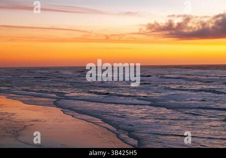 Il tramonto sull'oceano crea un cielo vibrante e un litorale riflettente sulla spiaggia Foto Stock