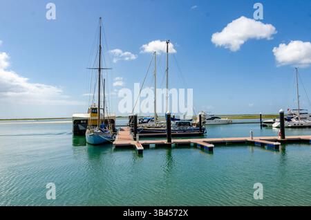 Barche a vela e a motore ormeggiate su un molo in una giornata di sole con cielo blu e nuvole Foto Stock