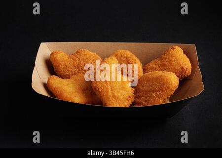 Croccanti pepite di pollo dorato servite in un vassoio di cartone su sfondo scuro, perfetto spuntino fast food. Foto Stock