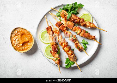Spiedini di satay di pollo malese con salsa di arachidi su sfondo bianco in cemento, vista dall'alto. Sate Ayam, cucina asiatica tailandese. Foto Stock