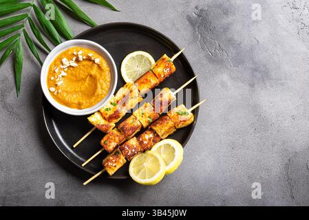 Spiedini in satay di tofu grigliati e salsa piccante alle arachidi su sfondo di cemento scuro, vista dall'alto, spazio copia. Pranzo vegetariano asiatico vegano, cucina tailandese. Foto Stock