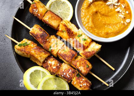 Spiedini satay di tofu grigliati e salsa piccante di arachidi su un piatto nero da vicino. Pranzo vegetariano asiatico vegano, cucina tailandese. Foto Stock