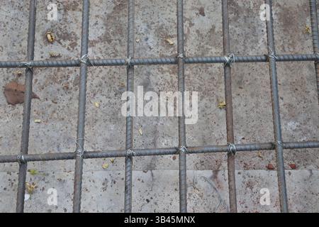 Ripresa ravvicinata con griglia di armatura fissata da filo metallico su una superficie di cemento preparata. Le barre in metallo arrugginite e nuove sono mostrate in forma quadrata Foto Stock