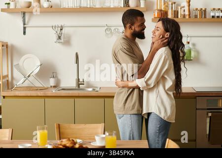 Una felice coppia nera condivide un amorevole abbraccio nella loro cucina. Foto Stock