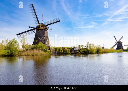 Vista panoramica di numerosi mulini a vento storici lungo i corsi d'acqua a Kinderdijk, Paesi Bassi, sotto un cielo blu con nuvole e riflessi. Foto Stock