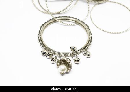 Presenta bracciali rigidi in argento, campane sospese, catene metalliche e un ornamento a forma di fiore con una perla su una superficie bianca pulita. Foto Stock