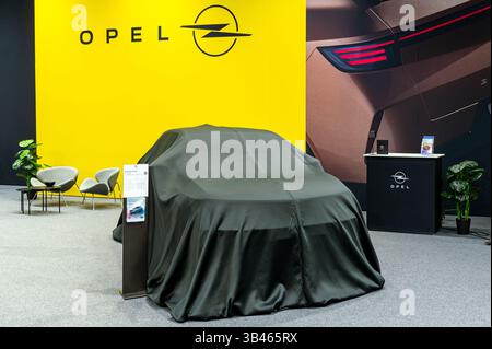 Riga, Lettonia - 25 aprile 2025: La nuova Opel Mokka coperta ti aspetta al salone dell'auto con uno sfondo audace e un display elegante. Foto Stock