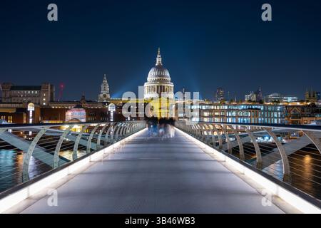 Il Millennium Bridge attraversa il Tamigi, illuminato sotto il cielo serale. La Cattedrale di San Paolo si erge maestosamente sullo sfondo, circondata dalle luci della città. Foto Stock