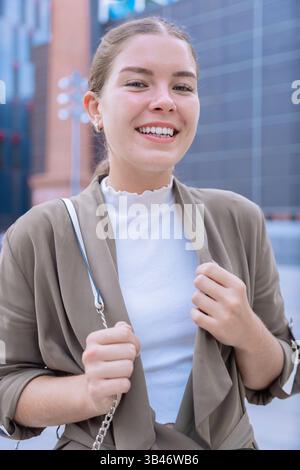 Primo piano felice ragazza caucasica che guarda la macchina fotografica e sorride ambientazione urbana Foto Stock