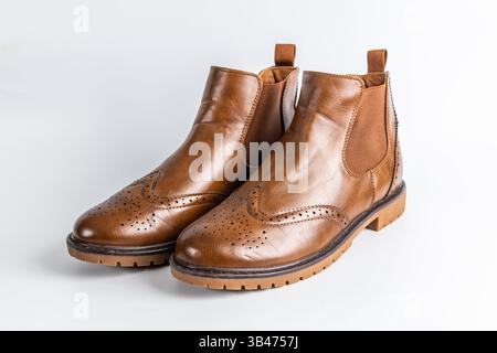 Un paio di stivali Chelsea marroni in pelle con dettagli in brogue e suola in gomma su sfondo bianco. Foto Stock