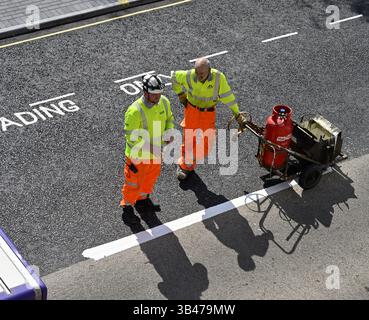 Due operai in abiti ad alta visibilità con macchina per verniciatura stradale Foto Stock