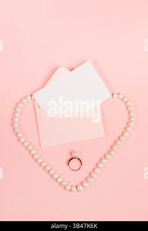 Disposizione stilizzata del matrimonio con invito, collana ad anello e perle a forma di cuore in rosa perfetta vista per San Valentino, fidanzamento, pubblicità romantica Foto Stock
