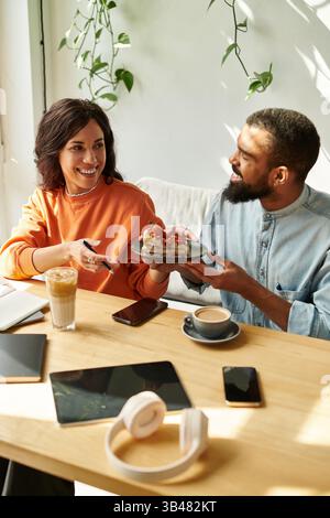 Una coppia afroamericana lavora insieme su progetti freelance mentre si gode una gustosa sorpresa. Foto Stock