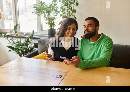 Una coppia afroamericana condivide risate e gioia mentre usa il telefono al chiuso. Foto Stock