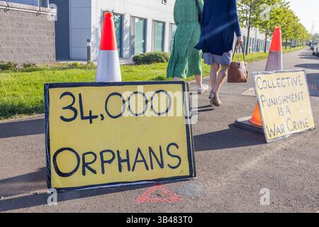 Samlesbury, Regno Unito. 30 APR, 2025. Le persone passano accanto al cartello "34.000 orfani" mentre i manifestanti hanno interrotto un evento educativo presso la BAE Academy for Skills and Knowledge nel Lancashire. L'evento è stato "pronto per il futuro: Padroneggiare la trasformazione digitale e le competenze per il successo". I manifestanti se ne sono andati di propria iniziativa intorno alle 11 del mattino. Si sa che la conferenza si è trasferita altrove, ma non sono stati in grado di utilizzare l'edificio originariamente previsto che conteneva dimostrazioni BAE dovevano mostrare ai partecipanti. Credito Milo Chandler/Alamy Live News Foto Stock