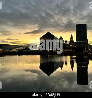 Lo skyline sul lungomare di Liverpool con il Royal Liver Building e il Museo di Liverpool si riflette nelle calme acque serali sotto un soffice cielo al tramonto. Foto Stock