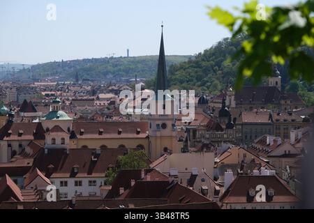 Vista della torre della chiesa che si erge sopra i tetti di tegole rosse nel centro storico di Praga, Repubblica Ceca, aprile 2025. Foto Stock