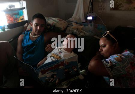 29 giugno 2015 - St. Petersburg, Florida, Stati Uniti - DIRK SHADD | Times.Black Students Achievement gap project:.Ivan Rivera-Otero (a sinistra) si arrampica a letto con il fratellino Derrick per guardare la televisione con lui e leggergli mentre la mamma Ermarie Otero viene al letto della loro casa mobile nel parco di casa mobile Sun Village di largo. (Foto scattata il 06/29/15).STORIA SOMMARIO: La famiglia di Ivan viveva vicino all'ospedale pediatrico in modo che il suo fratello disabile Derrick potesse ricevere cure mediche regolari. Ma dopo che Ivan e' stato vittima di bullismo alla Campbell Park Elementary School, sua madre ha dovuto scegliere tra Foto Stock
