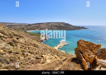 Vista panoramica di Golden Bay, Malta, con acque turchesi, colline costiere secche e bagni di sole su un affioramento roccioso nel mare. Foto Stock