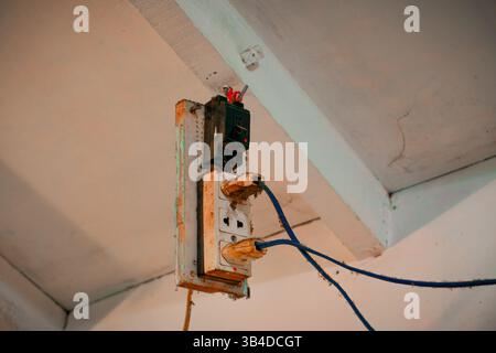 Presa elettrica arrugginita con fili esposti sul soffitto Foto Stock