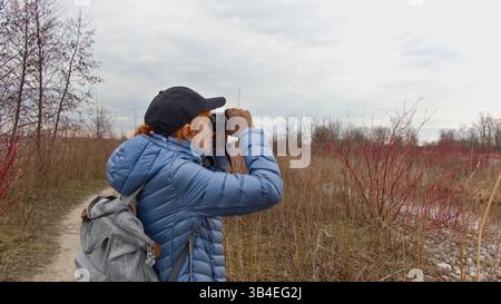 L'osservatore mirato si trova in sottobosco asciutto con binocolo, scansionando le cime degli alberi alla ricerca di uccelli all'inizio della primavera. Foto Stock