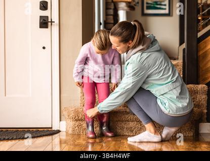 Madre che prepara suo figlio a lasciare la casa indossando le scarpe. Concetto di genitorialità Foto Stock