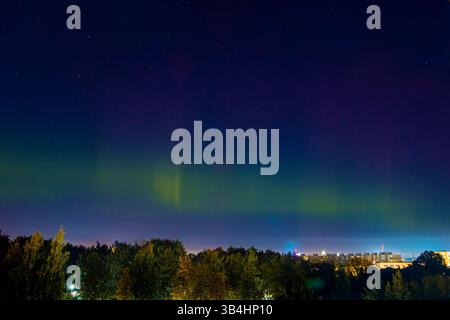 Aurora boreale sulla città. Luce pallida dell'aurora boreale nel cielo notturno. Il colore lampeggia nell'emisfero settentrionale. Foto Stock