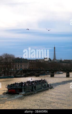 Barca sulla Senna al tramonto, con la Torre Eiffel in lontananza: Il fiume giallo e il cielo blu creano una splendida scena serale parigina. Foto Stock