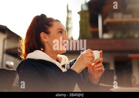 ragazza felice che tiene una tazza di espresso al tramonto sotto i raggi del sole Foto Stock