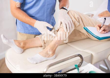 Il chirurgo insieme all'infermiera effettua un esame di una gamba dolorosa di una donna anziana in clinica Foto Stock