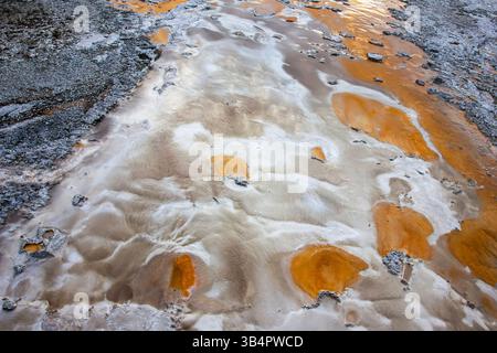 Colorati giacimenti di minerali sparsi in un sito geotermico all'interno di un parco nazionale. La miscela di tonalità arancio e grigio evidenzia texture uniche sulla g Foto Stock