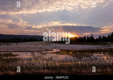 Uno splendido tramonto proietta un caldo bagliore sul parco nazionale di Yellowstone, mettendo in evidenza le caratteristiche geotermiche e il tranquillo riflesso in una zona umida vicina. Foto Stock