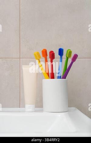Spazzolini multicolore. Sei spazzolini luminosi in vetro bianco in bagno con dentifricio. Arcobaleno. Igiene orale. Posiziona per testo. Rituale. Foto Stock