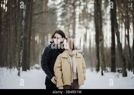 Una coppia in abiti caldi si trova in una foresta innevata, trasuda un'atmosfera serena Foto Stock