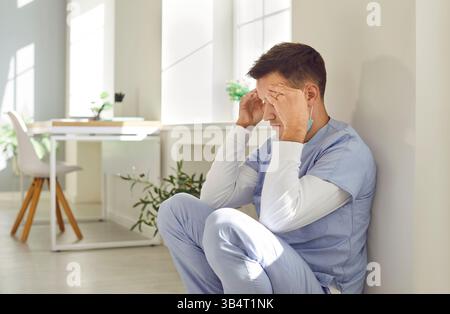 Un medico di sesso maschile stressato e stanco seduto a terra dopo una giornata di lavoro faticosa Foto Stock