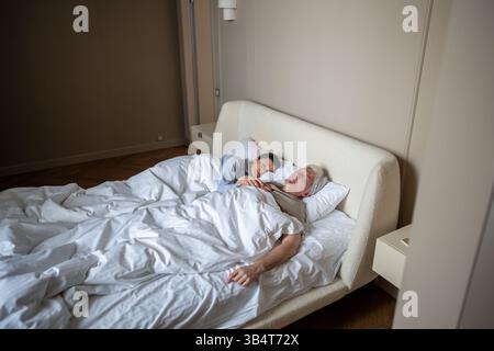 Marito e moglie maturi e tranquilli dormono sonni tranquilli mentre si abbracciano insieme in un'accogliente camera da letto Foto Stock