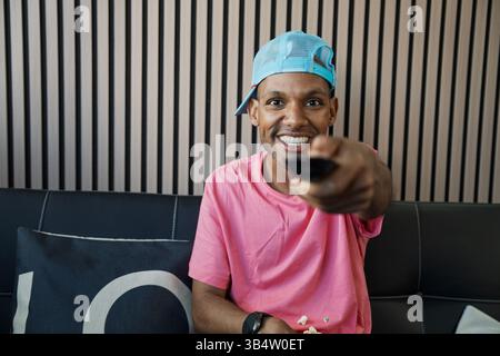 Uomo sorridente che guarda la televisione e cambia canale, seduto comodamente su un divano Foto Stock
