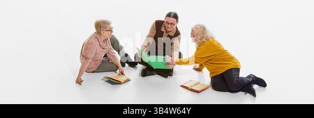 Banner, volantino. Tre donne anziane che leggono e discutono libri sul pavimento su sfondo bianco in studio. Studio di gruppo. Condivisione delle conoscenze Foto Stock