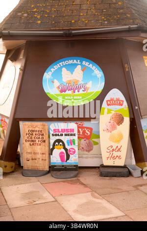 Banco gelati con tantissimi cartelli pubblicitari che mostrano i tipi di gelato che vendono a Teignmouth, Devon, Inghilterra Foto Stock