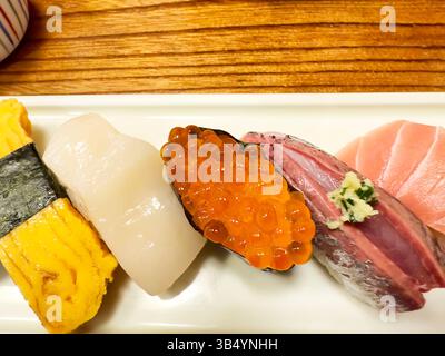 Vista dall'alto di vari sushi giapponesi che consistono di pesce, uova e gamberi in un piccolo piatto bianco Foto Stock