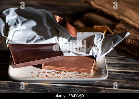Tavolette di cioccolato fondente e al latte su un piatto, cioccolato artigianale, su un tavolo di legno con sfondo rustico. Foto Stock