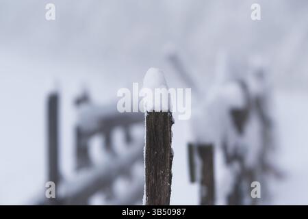 Palo in legno di stecca per bestiame con deriva della neve sulla parte superiore, recinzione curvata con filo spinato, paesaggio invernale Foto Stock