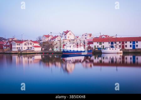 Una tranquilla vista del porto di Kladesholmen in Svezia all'alba. Le barche da pesca sono attraccate pacificamente mentre le case colorate si riflettono nelle acque calme, c Foto Stock